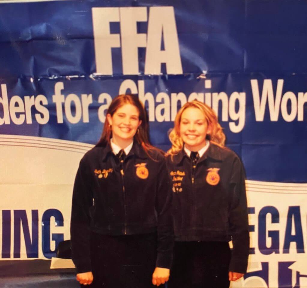 two girls in navy jackets pose before a banner 