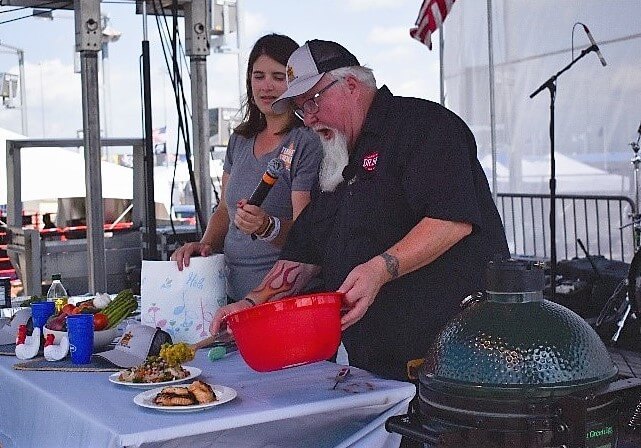 Dr. BBQ holding a red bowl onstage with a table 