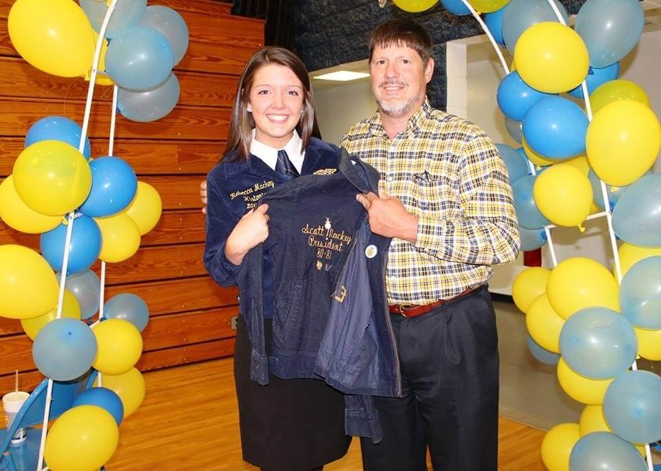 Student and father pose for a photo under yellow and blue balloons 