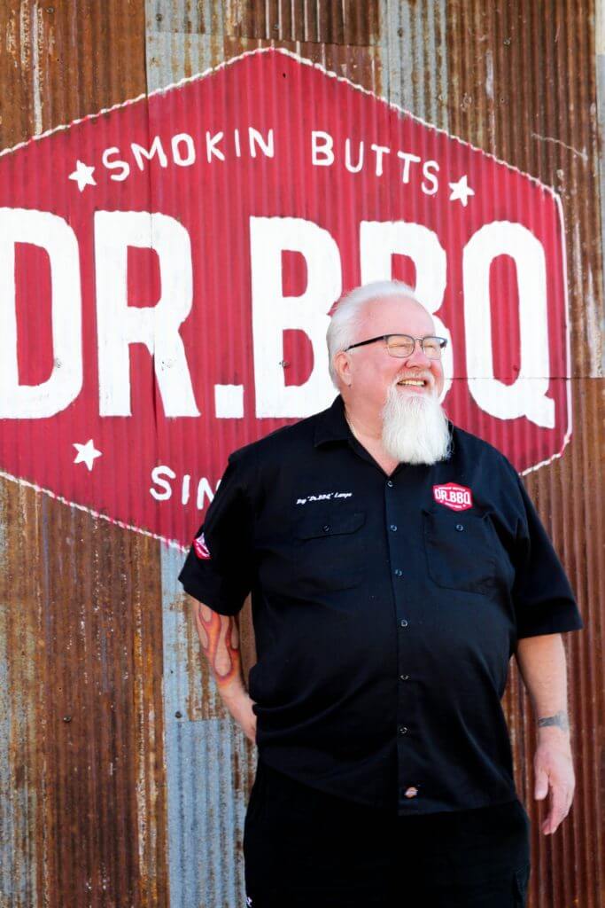 Dr. BBQ in front of a red sign 