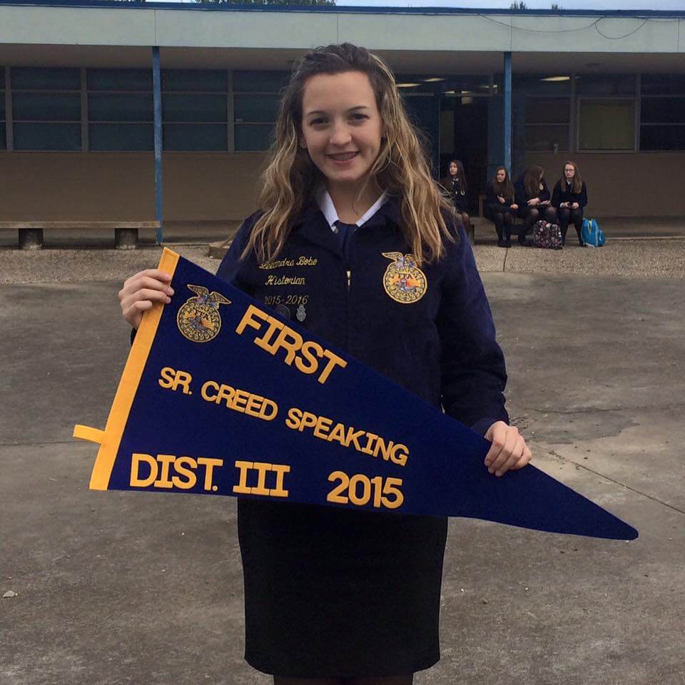 Student in navy jacket poses with navy pennant 